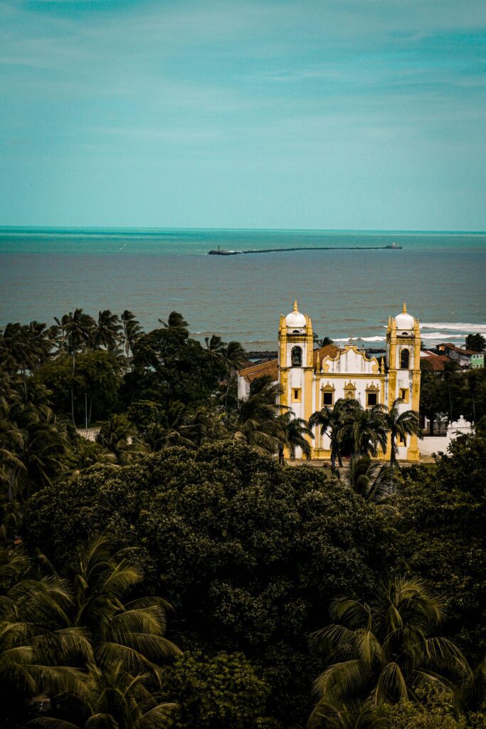 Photo d'Olinda au Brésil : vue de haut sur une église avec la mer et le forêt l'entourant.