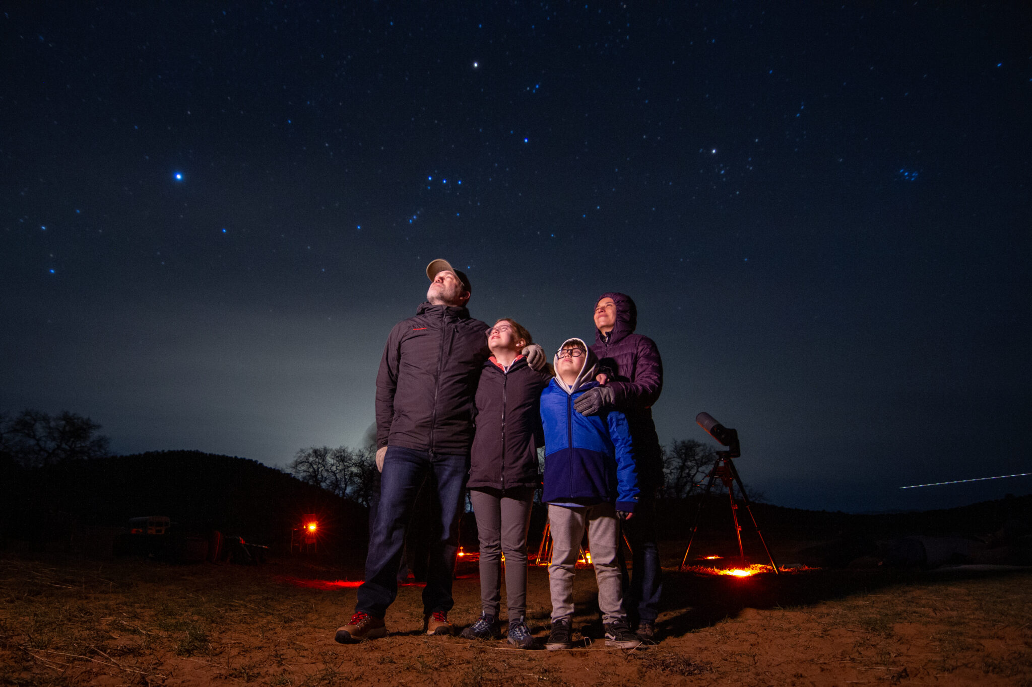 Une famille de 4 ( 2 parents et 2 enfants) regardant les étoiles en pleine nuit.