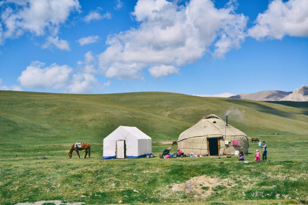 Plaine avec des yourtes et chevaux au Kirghizistan, avec un ciel bleu et des nuages.