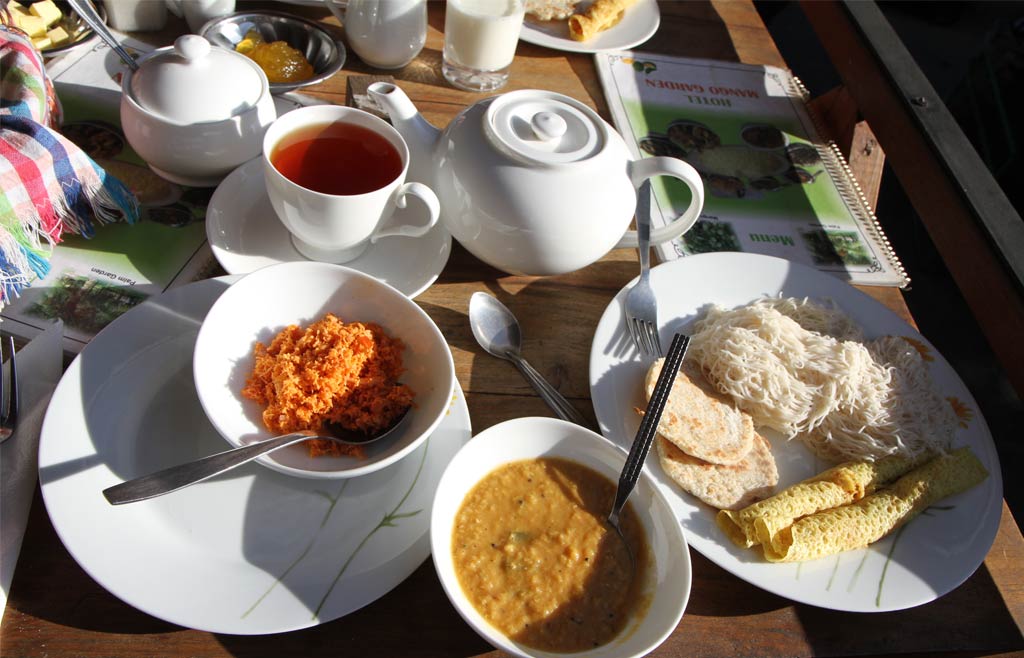 Table remplie de petit déjeuner, avec de la nourriture Sri Lankaise et du thé