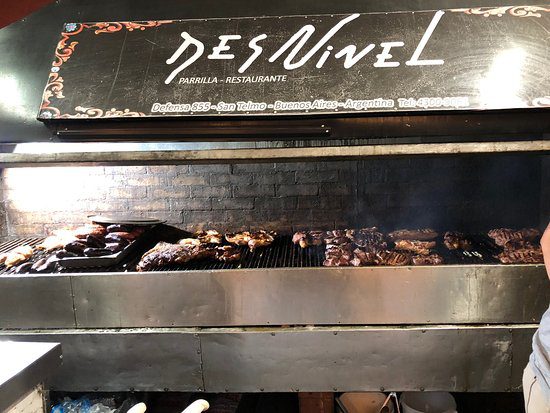 Viandes cuisants sur les plaques de cuissons du restaurant "desninels" avec leur logo sur une planche au dessus.