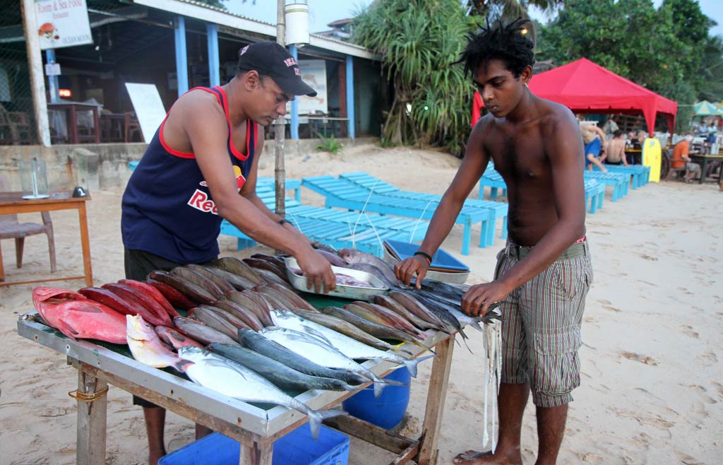 Un vendeur de poisson sur un marché de plage, avec un acheteur en rpemier plan.