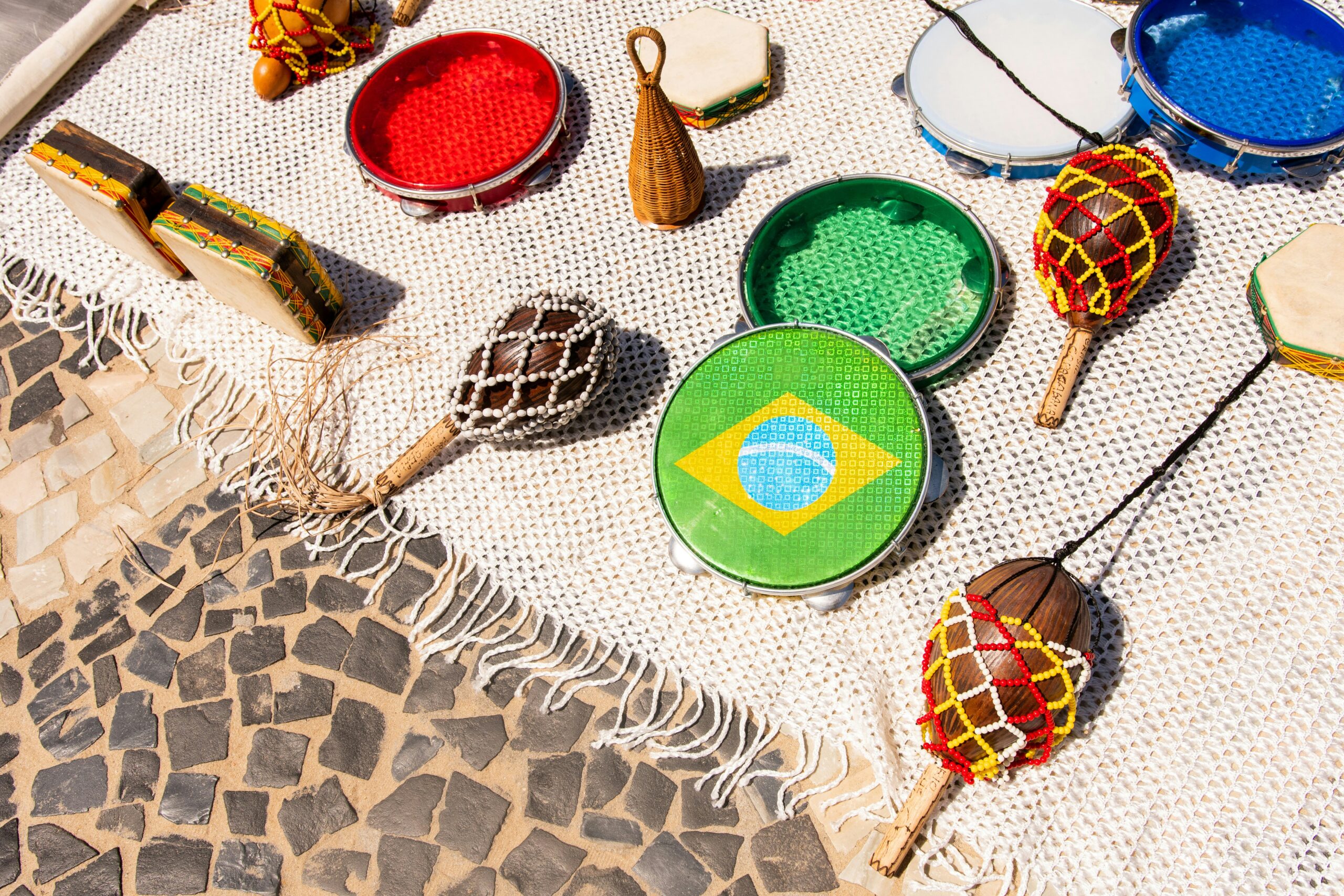 Multiples instruments de musique (samba, forro, bossa nova...), sur un paréo, dont un instrument avec le drapeau brésilien dessus.