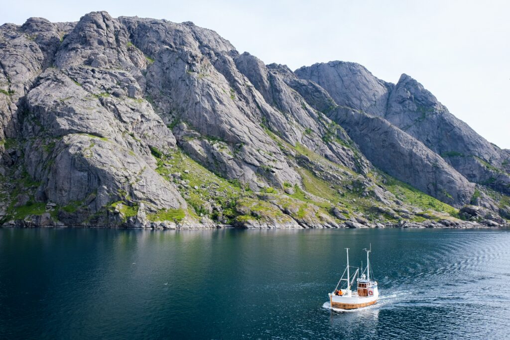 nusfjord norvege : montagne en fond, bateau navigant sur un lac en premier plan.