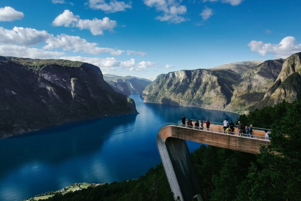Personnes sur un ponton en hauteurs d'une montagne admirant la vue d'aurland en Norvège (montagnes entourant un lac)