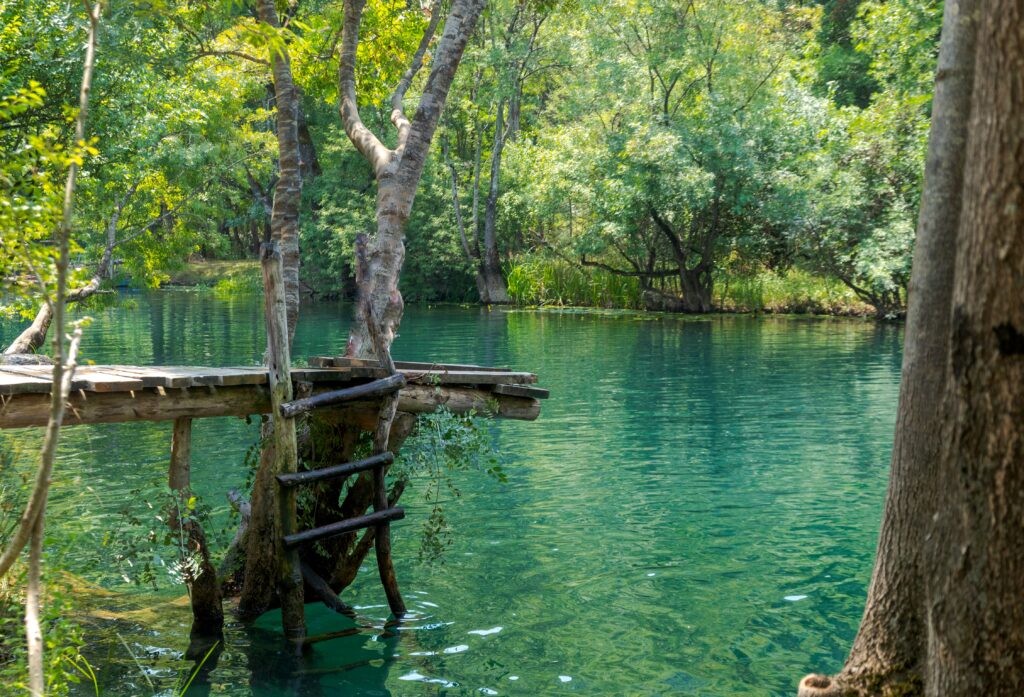 Lac à Trebinje entouré d'arbres, avec un petit ponton pour aller dans l'eau au premier plan.