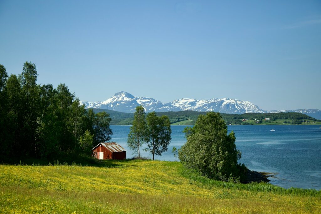 Maison sur une plaine devant un lac, montagne en arrière-plan.