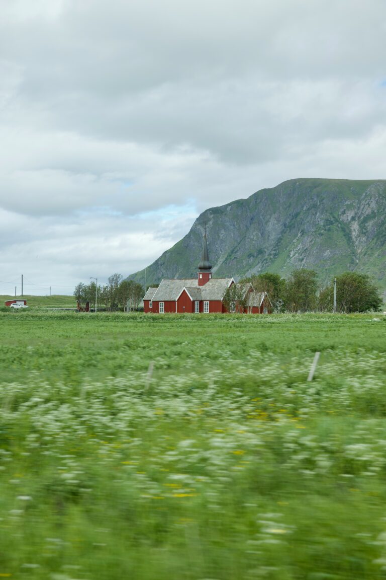 Maison rouge centrée sur une plaine avec une montagne en arrière-plan.